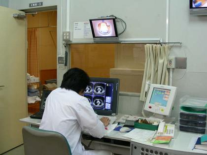 CT撮影が行われている検査室内を窓越しに見守る放射線技師。モニターと同時に細心の注意を払う